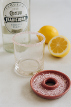 Load image into Gallery viewer, Tequila bottle, glass with salt rim, and lemons on a light surface
